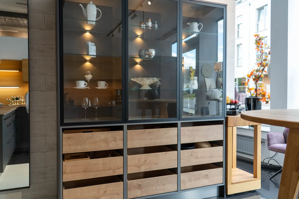 Beleuchtete Glasvitrine mit Geschirr und Schubkästen